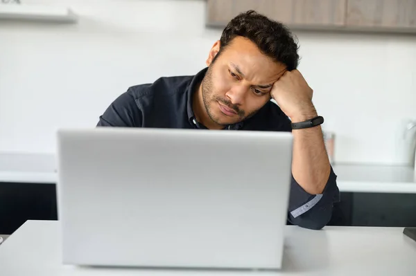 Homem multi-étnico perturbado está usando laptop sentado em casa sozinho — Fotografia de Stock