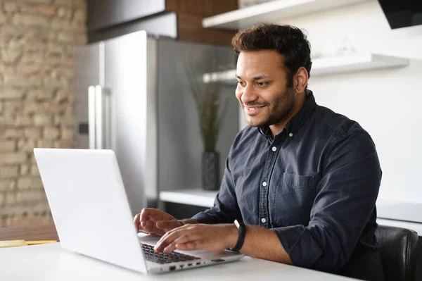 Smiling young indian guy using a laptop for remote work from home