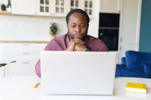 Enfocado y preocupado hombre negro en camisa casual inteligente mira a la pantalla del ordenador portátil — Foto de Stock