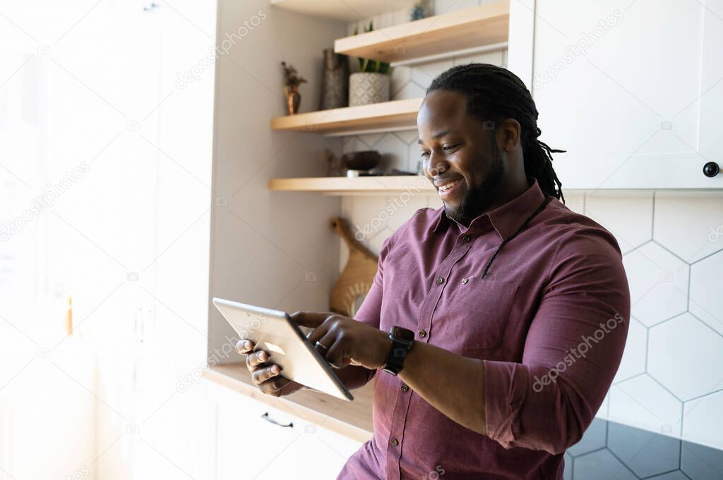 Joyful and positive African-American guy scrolling on touchscreen of digital tablet
