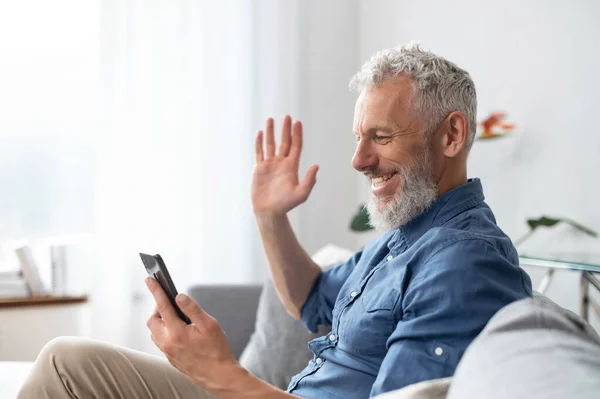 Бородатий чоловік середнього віку використовує смартфон для відеодзвінків — стокове фото