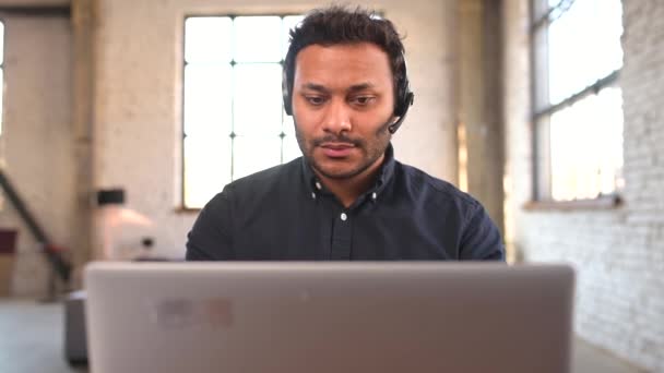 Concentrated hindu man wearing wireless headset using laptop for remote connection — Stock Video