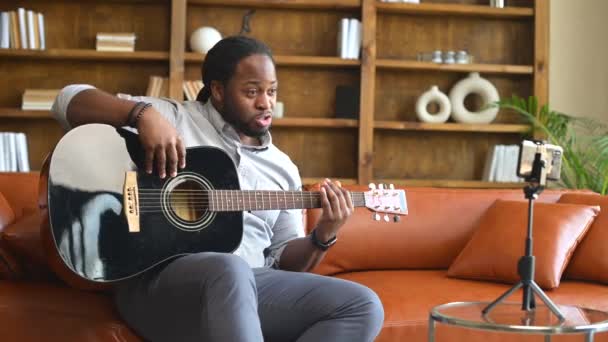 Ein afroamerikanischer Mann spielt Gitarre vor einem Smartphone — Stockvideo