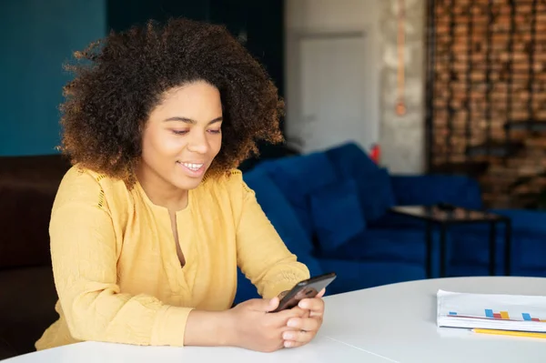 Ung afroamerikansk kvinna använder smartphone hemma — Stockfoto