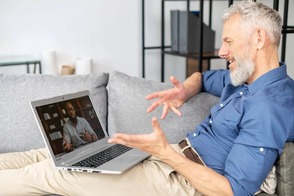 Mature bearded man talking online via video connection on the laptop