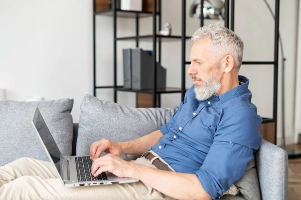 Bärtiger Mann mittleren Alters legt sich mit Laptop auf die Couch — Stockfoto