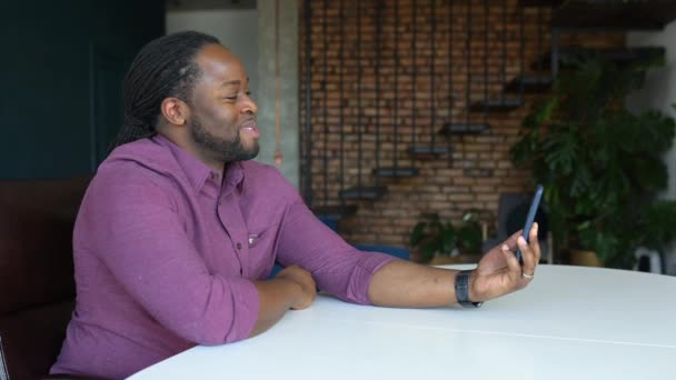 Positivo y alegre chico afroamericano hace videollamada por el teléfono inteligente — Vídeos de Stock