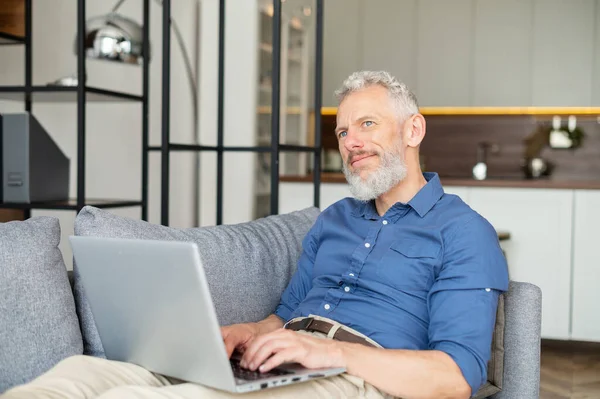 Senior freelancer di sesso maschile sdraiato sul divano e utilizzando il computer portatile — Foto Stock