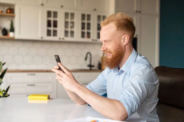 Vista lateral de hombre caucásico de pelo rojo guapo usando teléfono inteligente — Foto de Stock