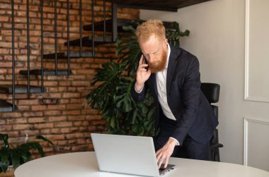 Sorumlu kızıl saçlı, takım elbiseli iş adamı akıllı telefondan konuşuyor.