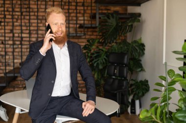 Gülümseyen kızıl saçlı, yetenekli bir lider akıllı telefondan konuşuyor.