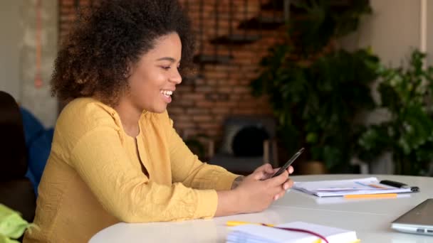 Afro-Amerikalı kadın evdeki masada oturuyor ve akıllı telefon kullanıyor. — Stok video