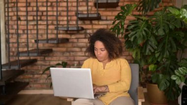 Çekici, mutlu, genç, Afro-Amerikan bayan girişimci uzaktan kumanda için dizüstü bilgisayar kullanıyor.