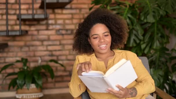 Jonge Afro-Amerikaanse vrouw die op de fauteuil zit te lezen — Stockvideo