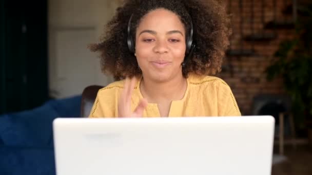 Веселая афроамериканка в наушниках разговаривает онлайн с коллегами или клиентами — стоковое видео