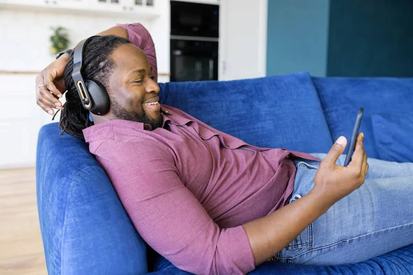 Africano hombre en auriculares pasa tiempo libre viendo películas en el smartphon — Foto de Stock