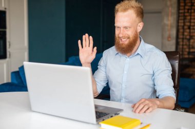 İyimser kızıl sakallı iş adamı laptopta video görüşmesi yapıyor.