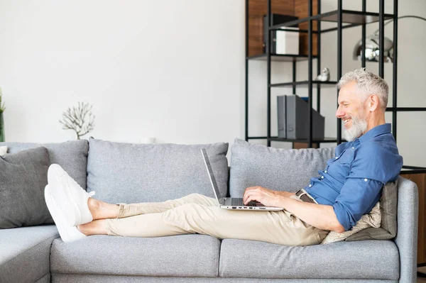 Orta yaşlı sakallı bir adam elinde dizüstü bilgisayarla kanepeye uzandı.