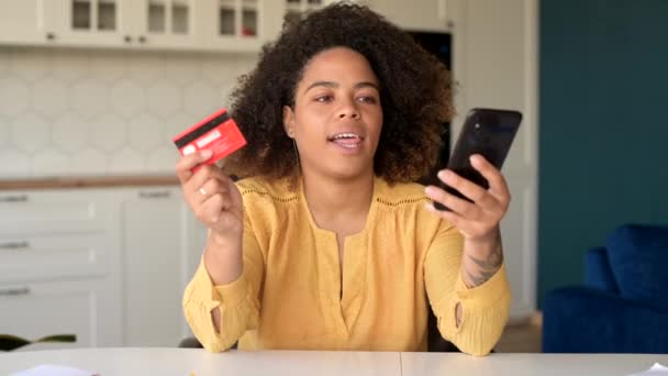 Ενθουσιασμένη νεαρή Αφροαμερικανή γυναίκα κατέχει smartphone και πιστωτική κάρτα — Αρχείο Βίντεο