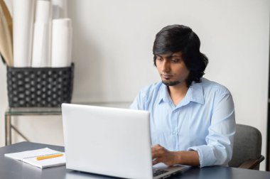 İç dizüstü bilgisayar kullanan akıllı, rahat gömlekli bir Hintli.