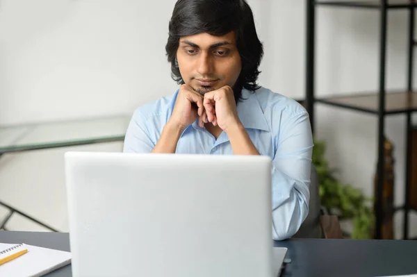 Focused clever indian man in smart casual shirt using laptop indoor