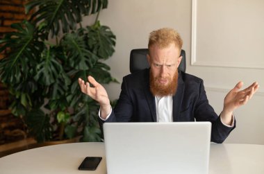 Şaşırmış ve kafası karışmış kızıl sakallı iş adamı dizüstü bilgisayara bakıyor.