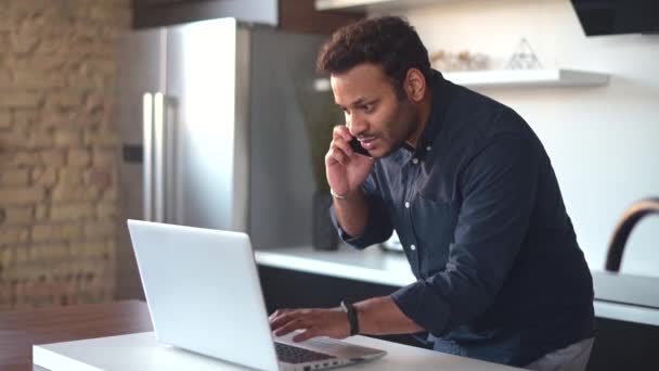 Young man checking something on the laptop during phone conversation — Stock Video