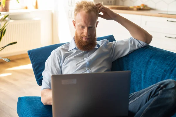 Un uomo trascorre il tempo libero in rete sdraiato sul divano — Foto Stock