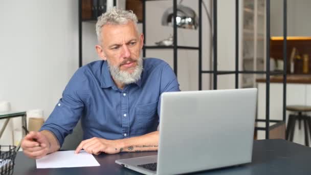 현대식 중년의 수염을 기른 남자가 가정 사무실에서 노트북을 가지고 일하고 있다 — 비디오