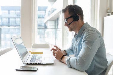 Kendine güvenen bir erkek ofis çalışanı masada dizüstü bilgisayarla oturuyor.