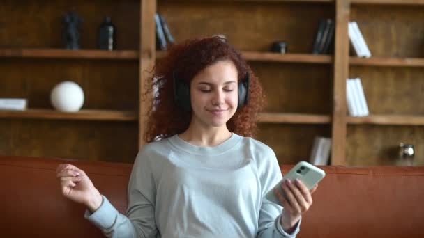 Sereno joven pelirroja rizada con auriculares disfruta de pistas favoritas — Vídeos de Stock