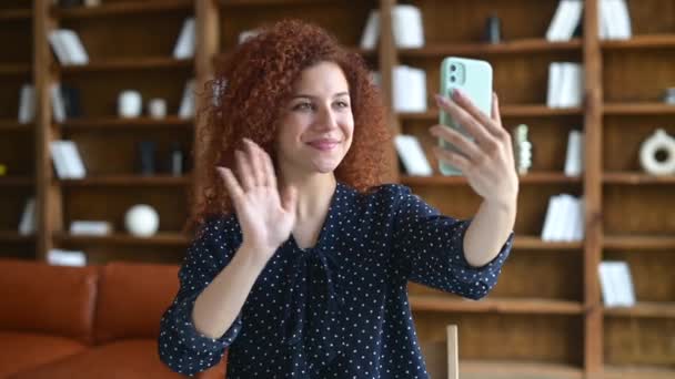 Sonriendo rizado empleado femenino tiene videollamada en el teléfono inteligente — Vídeos de Stock