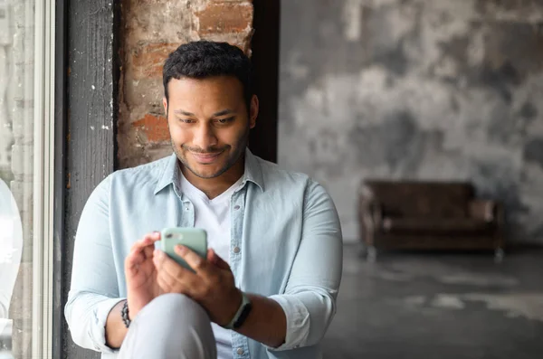 Hombre de pelo oscuro indio feliz y sonriente con camisa casual usando teléfono inteligente —  Fotos de Stock
