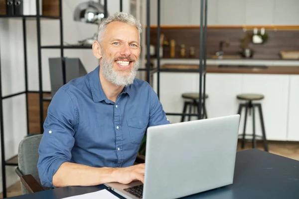 Ritratto di uomo maturo dai capelli grigi che utilizza il computer portatile in home office — Foto Stock