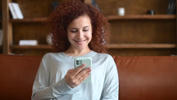 Joven mujer de pelo rojo rizado charlando por teléfono y sonriendo ampliamente — Vídeo de stock