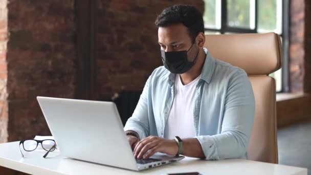 Indischer Mann mit einer medizinischen Schutzmaske auf dem Gesicht sitzt im Büro — Stockvideo