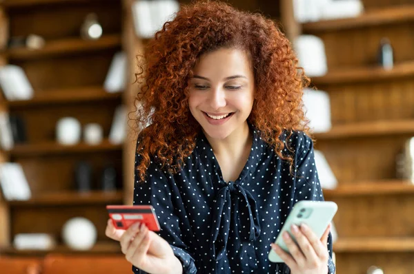 Krullende vrouw in casual shirt met credit bank kaart en smartphone — Stockfoto