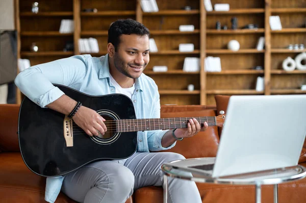 Sonriente joven indio aprendiendo a tocar la guitarra en línea —  Fotos de Stock