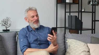 Mutlu orta yaşlı adam akıllı telefondan video görüşmesi yapıyor.