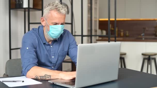 Ältere grauhaarige männliche Angestellte mit medizinischer Maske benutzt Laptop im Büro — Stockvideo