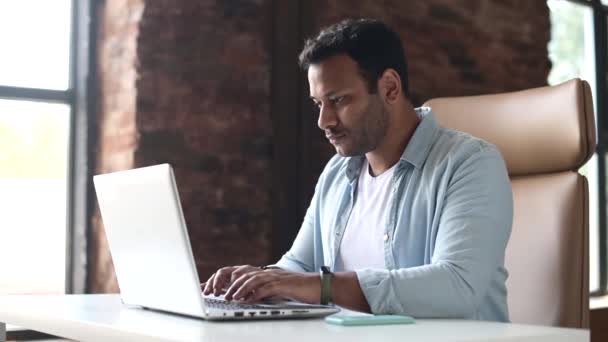 Desesperado índio jovem funcionário do sexo masculino sentado na mesa e usando laptop — Vídeo de Stock