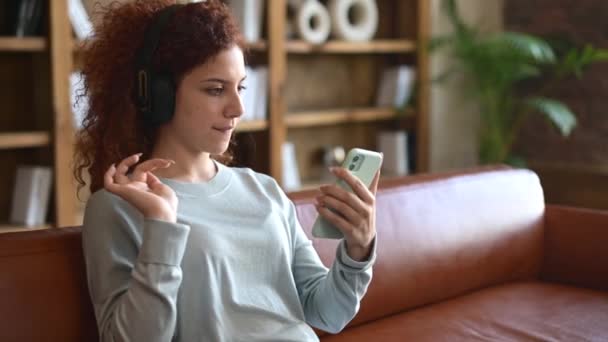 Joyful encaracolado jovem ruiva mulher usando fones de ouvido sem fio gostando de ouvir música — Vídeo de Stock