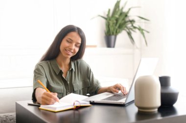 Gülümseyen Hintli kız öğrenci bilgisayar kullanarak webinarları izliyor.