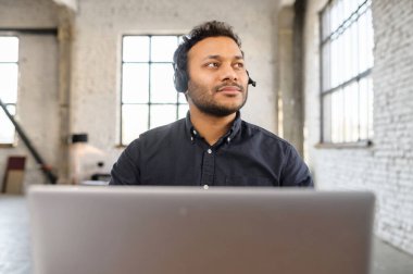 Modern ofiste kulaklık kullanan Hintli adam.