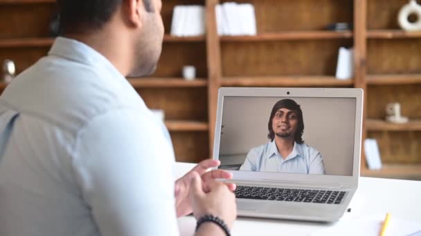 Two indian male office employee greeting each other, talking online via video connect on a laptop — ストック動画