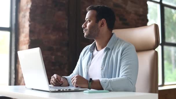 Optimistische Indiase knappe man draagt casual shirt met laptop voor het werk — Stockvideo