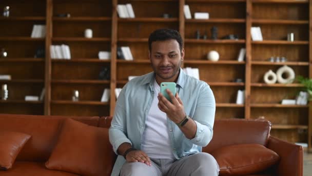 真剣に焦点を当てたインド人男性でカジュアルウェアを使用してスマートフォンアプリのためのビデオ通話 — ストック動画