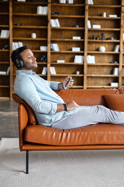 Indian guy takes a break and resting lying on the sofa and listening music