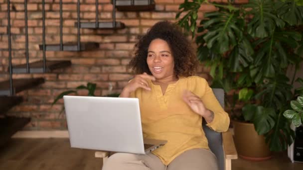 Encantadora mujer afroamericana sentada en el sillón, saludando al portátil — Vídeo de stock