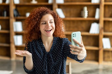 Gülümseyen kıvırcık kadın çalışanın akıllı telefonunda görüntülü arama var.